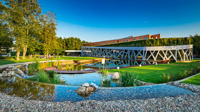Widok zewnętrzy na Hotel Narvil. Na pierwszym planie oczko wodne i drobne kamienie, w tle hotel posiadający liczne sale konferencyjne.